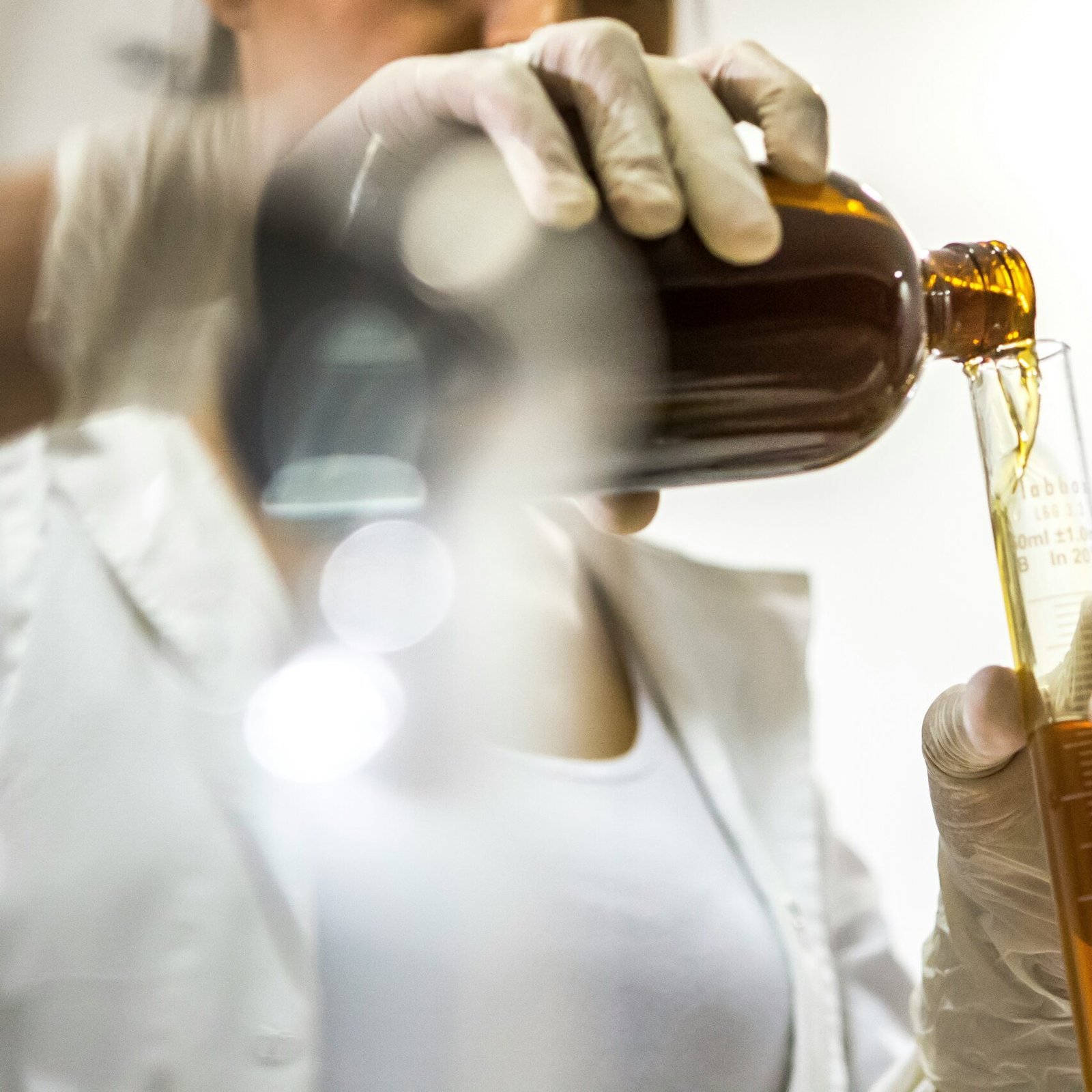 woman wearing white lab coat holding brown bottle and glass tube